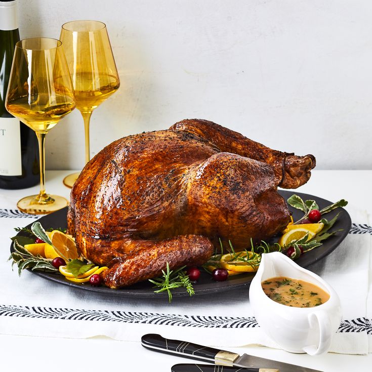 a roasted turkey on a platter with wine glasses and utensils next to it