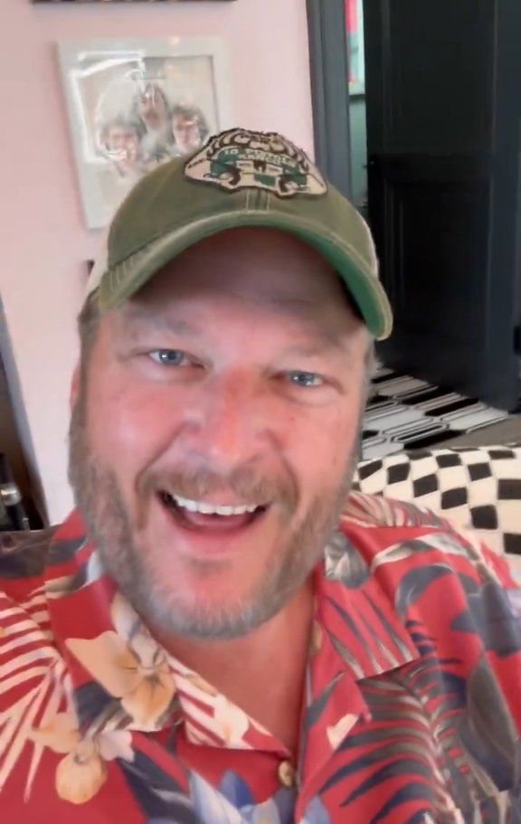 a man with a beard wearing a red shirt and green hat smiling at the camera