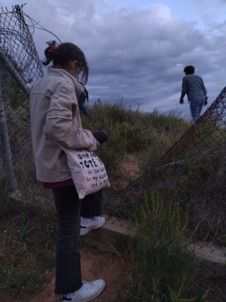 two people walking up some stairs with barbed wire on the top and one person carrying a bag