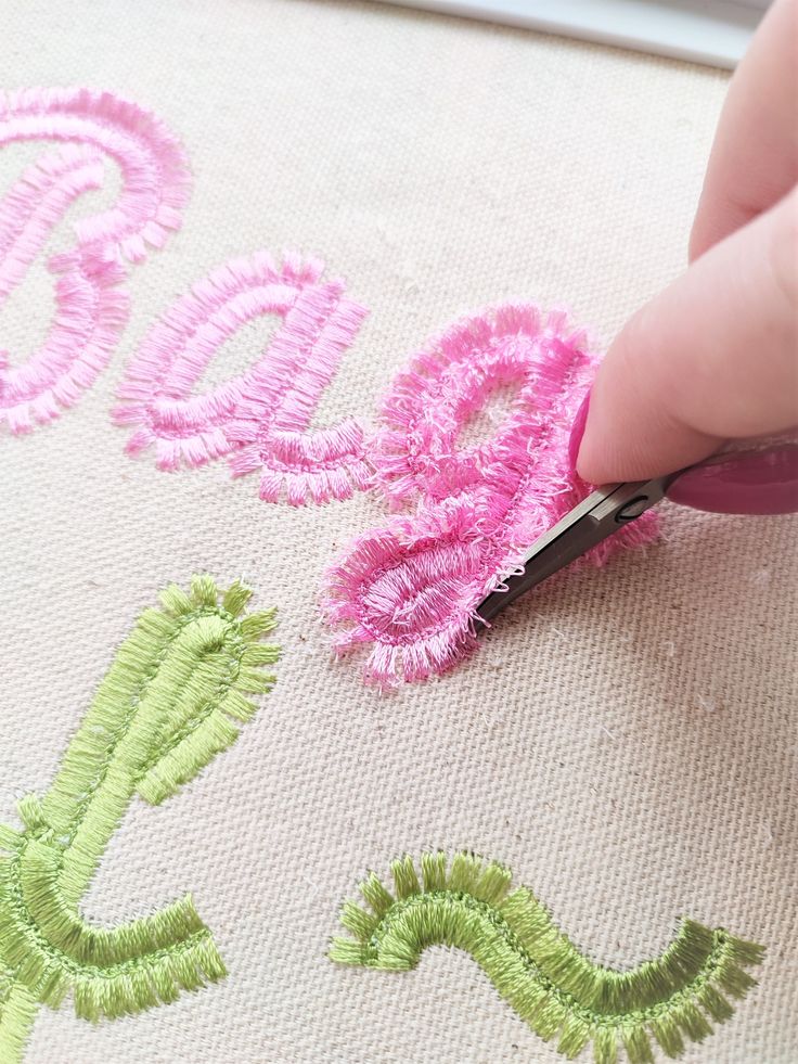 someone is doing something with pink and green thread on the fabric that has been embroidered onto