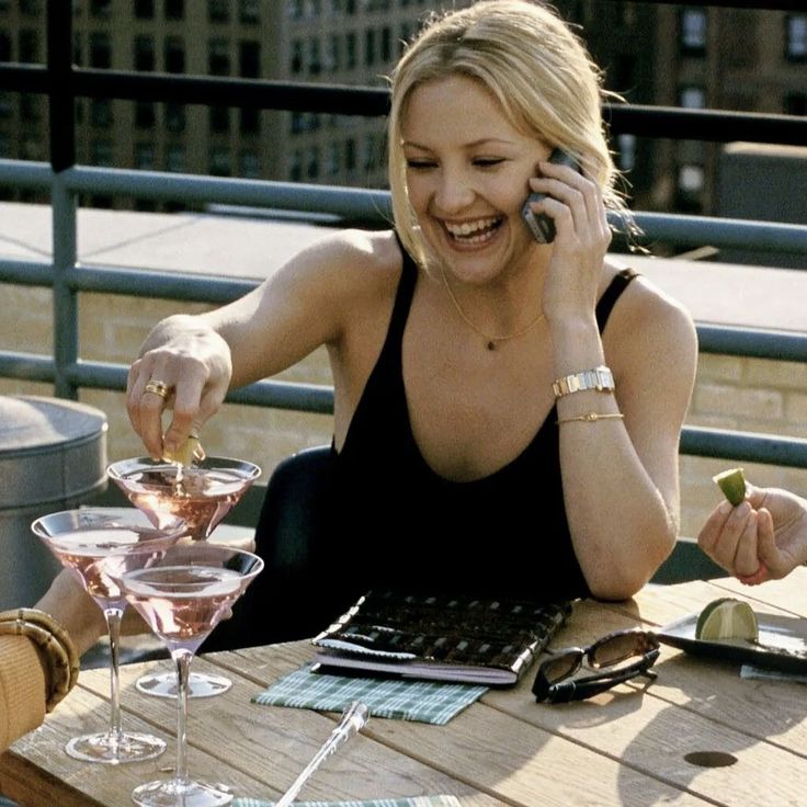 a woman sitting at a table talking on a cell phone and holding a drink in her hand