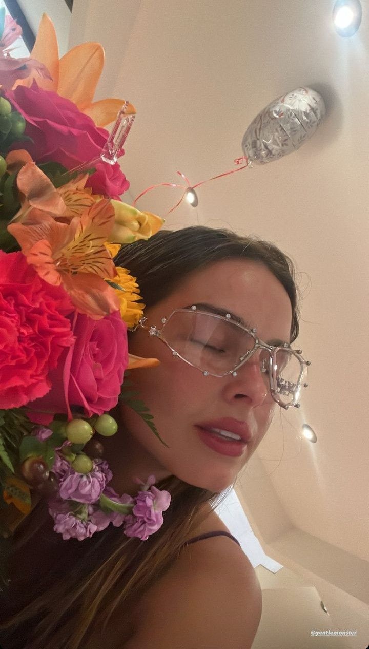 a woman wearing glasses with flowers on her head in front of a mirror and lights