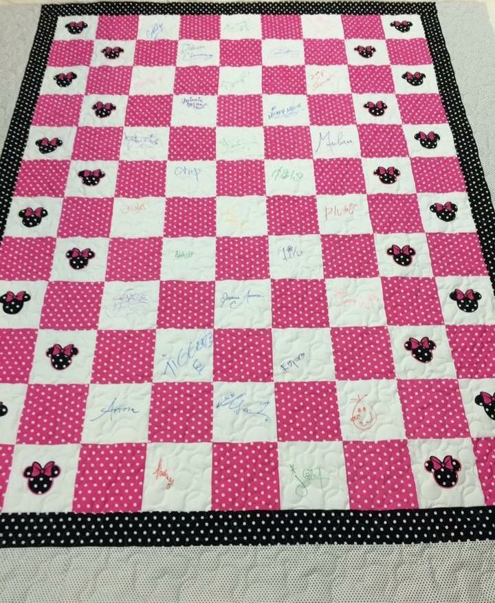 a pink and black checkered quilt with minnie mouses on the front, along with handwritten autographs