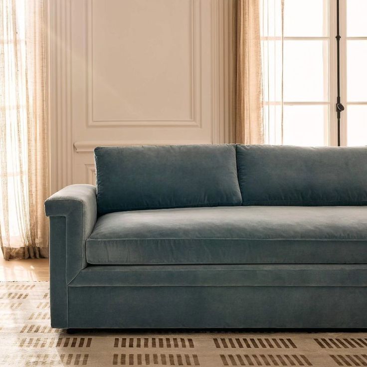 a blue couch sitting on top of a wooden floor next to a white wall and window