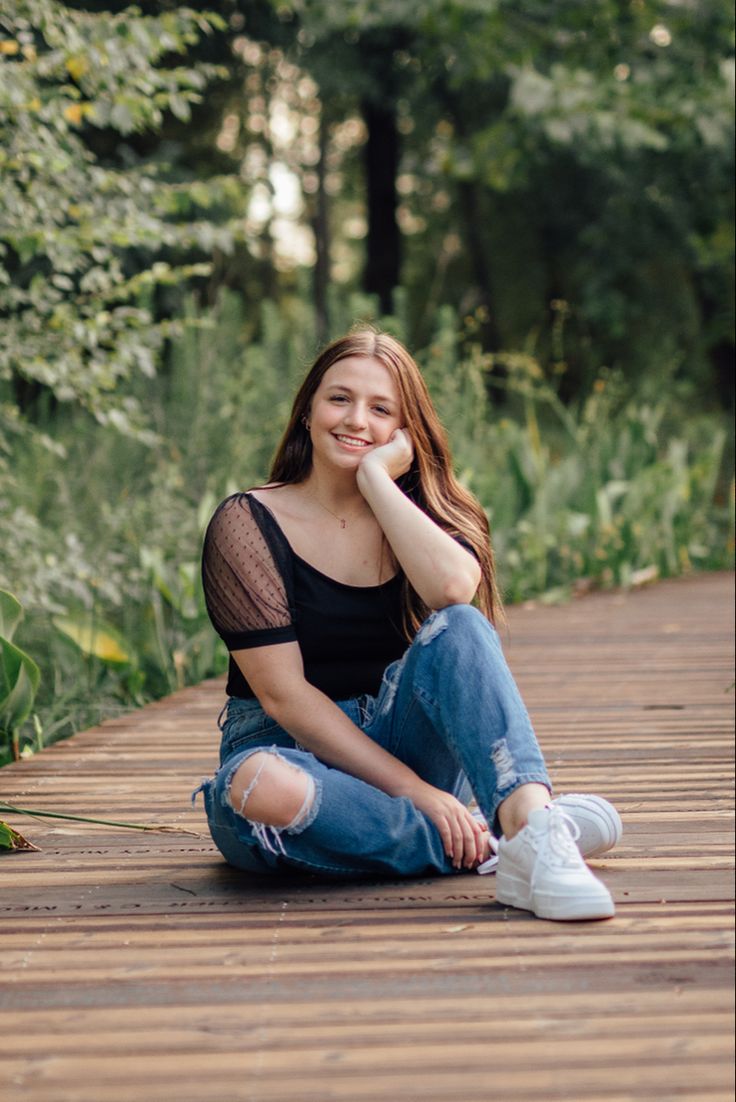 a young woman sitting on the ground with her legs crossed and looking at the camera