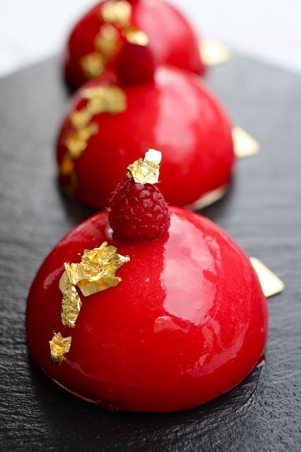 three chocolate covered desserts with raspberries and gold leaf decorations