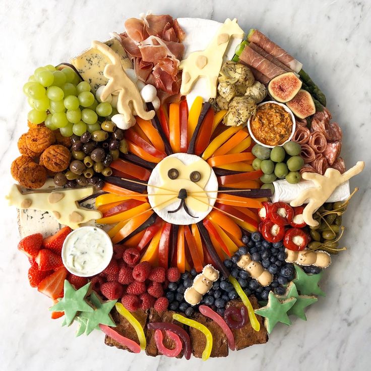 a circular platter filled with fruits and vegetables, including grapes, carrots, meats, cheeses, and other foods