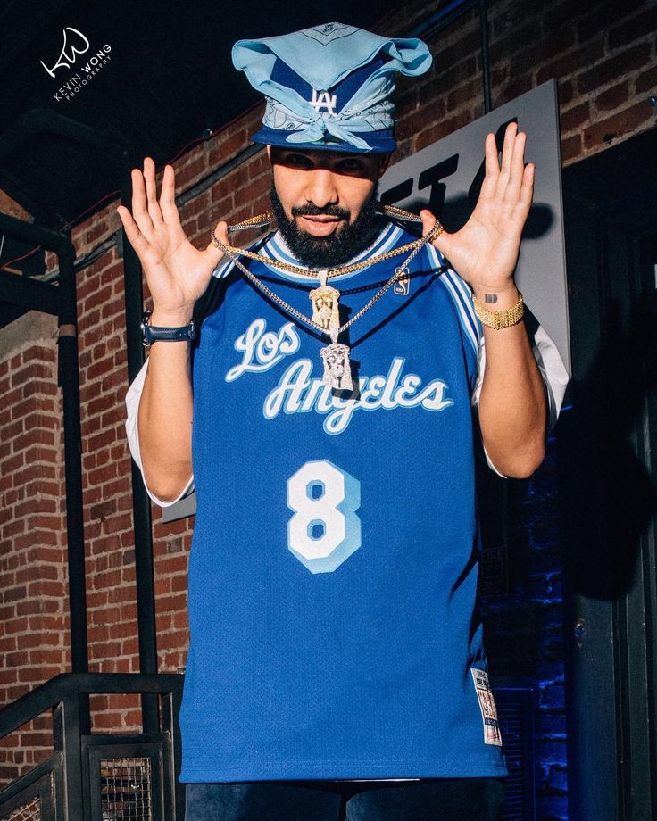 a man in a blue jersey and hat holding his hands up to the side while standing next to a brick wall