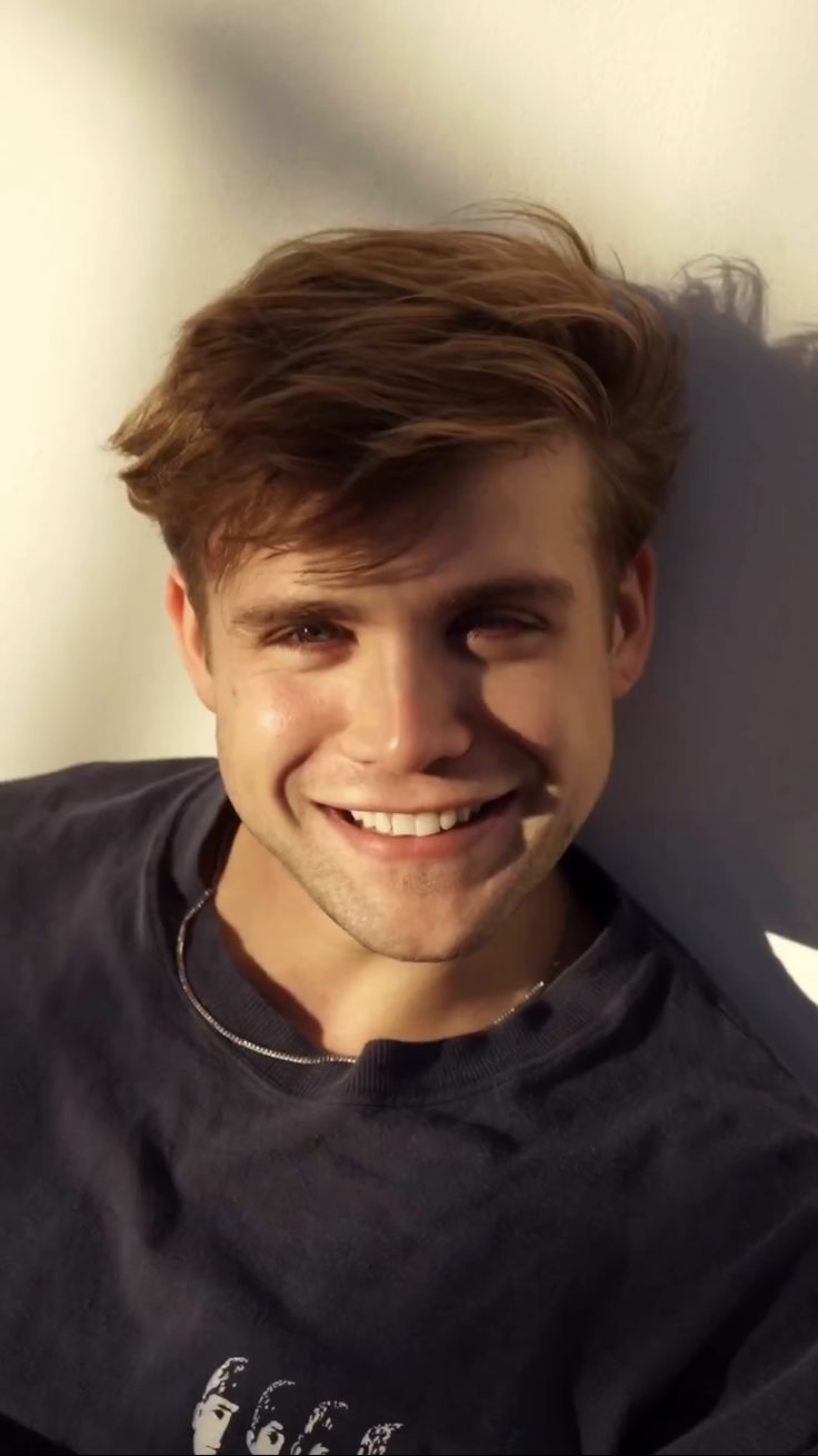 a young man smiling and leaning against a wall with his head turned to the side