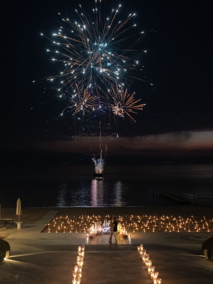 fireworks are lit up in the night sky above a walkway leading to an ocean side wedding venue