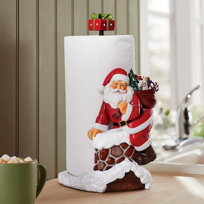 a santa clause figurine sitting on top of a counter next to a roll of toilet paper