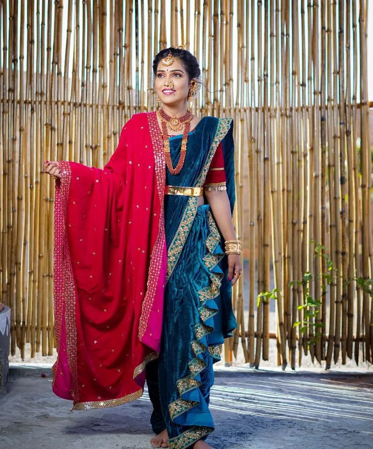 a woman in a blue and red sari standing next to bamboo wall with her hand on her hip