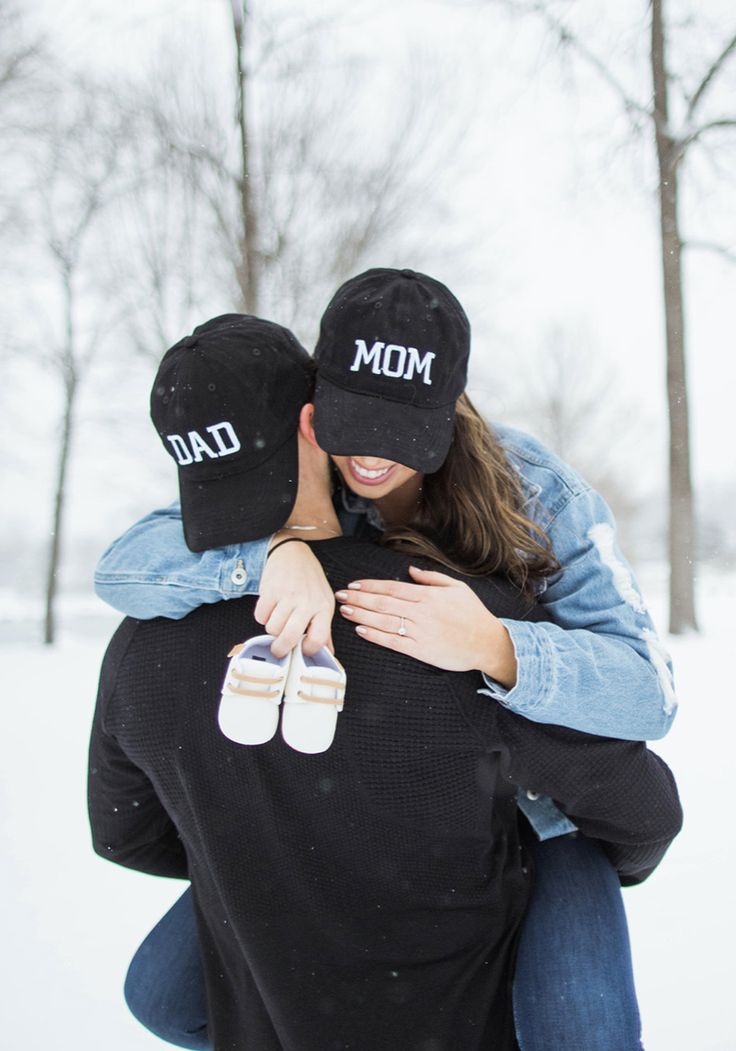 a man and woman hugging each other in the snow wearing baseball caps that read mom