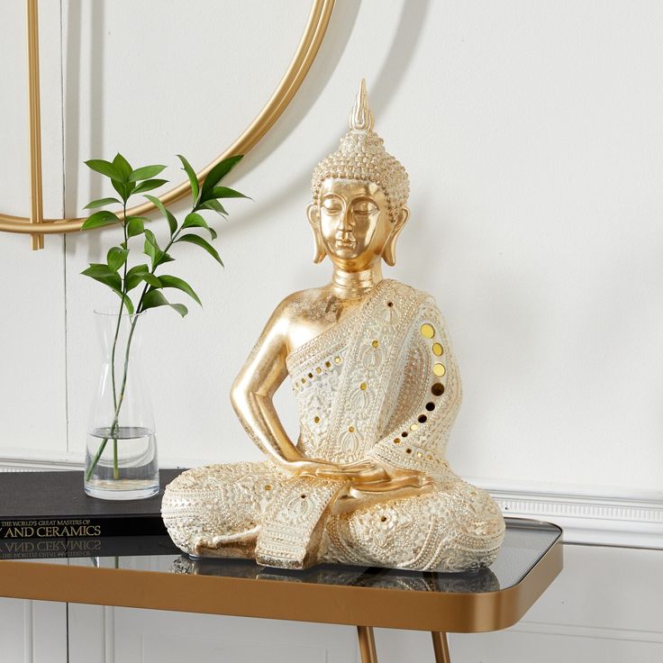 a gold buddha statue sitting on top of a table next to a vase with a plant