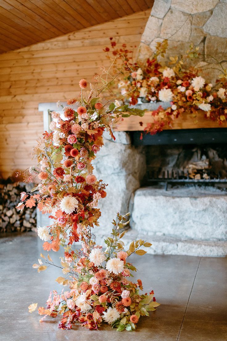 an arrangement of flowers on the floor in front of a fire place with logs and fireplace