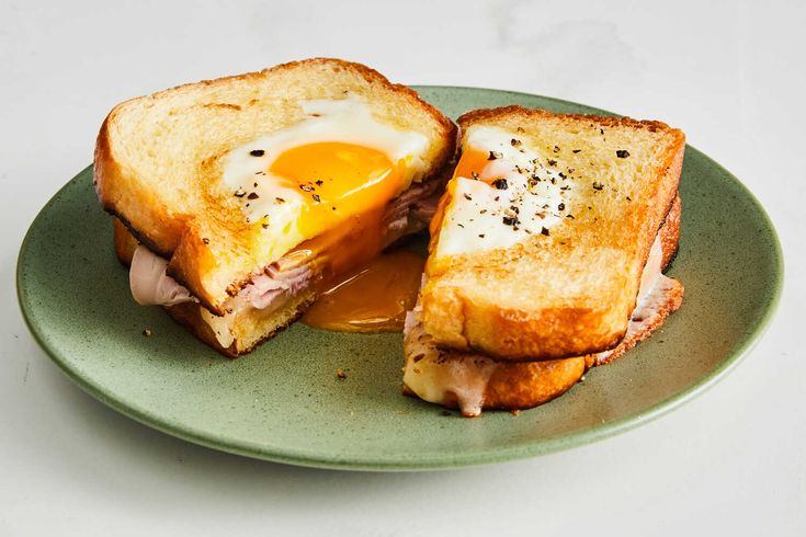 a sandwich with an egg in the middle is on a green plate and sits on a white surface