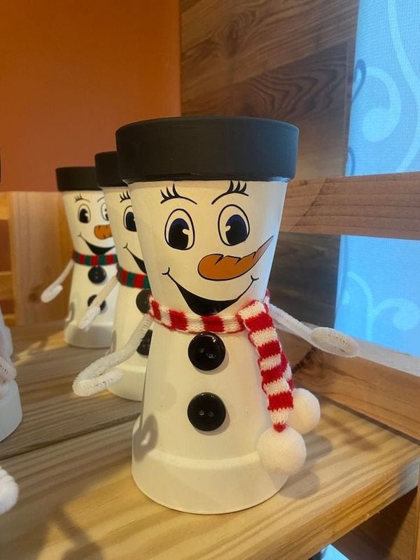 three snowmen with hats and scarves are sitting on a wooden table in front of a window