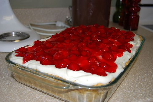 a cake with white frosting and red toppings in a glass dish on a counter