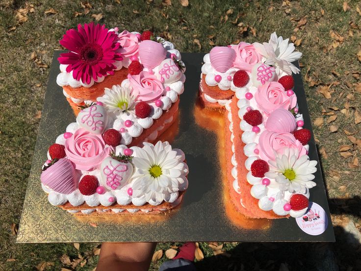 two cakes decorated with flowers and hearts are on a table in front of someone's hand