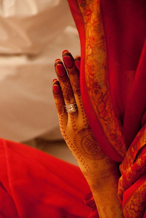 a woman's hand with henna on her left and red fabric draped around her