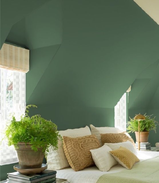 a bedroom with green walls and white bedding, potted plants on the nightstand