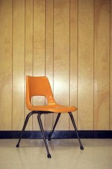 an orange plastic chair sitting in front of a wooden paneled wall with black legs