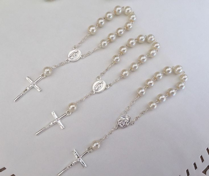 "Beautifully made minirosaries perfect for baptism favor/ or communion favor. They are small rosaries made in elegant off white acrylic pearls in 6mm round smooth beads. Featuring the image of our lady of Guadalupe on the center piece, a solid center piece matching a solid metal crucifix , accents are silver plated. They measure just a bit over 4.5\" inches long. They are not bracelets, they are mini rosaries. Si tiene pregunta con gusto le atenderemos ." Silver Baptism Jewelry With 8mm Beads, Personalized Silver Rosary For Confirmation, Elegant Silver Rosary As Gift, Pearl White Rosary With 8mm Beads As Gift, Silver Pearl Rosary With 8mm Beads, Silver Jewelry With 8mm Beads For Baptism, Silver Pearl Rosary For First Communion, Elegant Silver Rosary Bracelet For Baptism, Silver Pearl Rosary Bracelet For First Communion