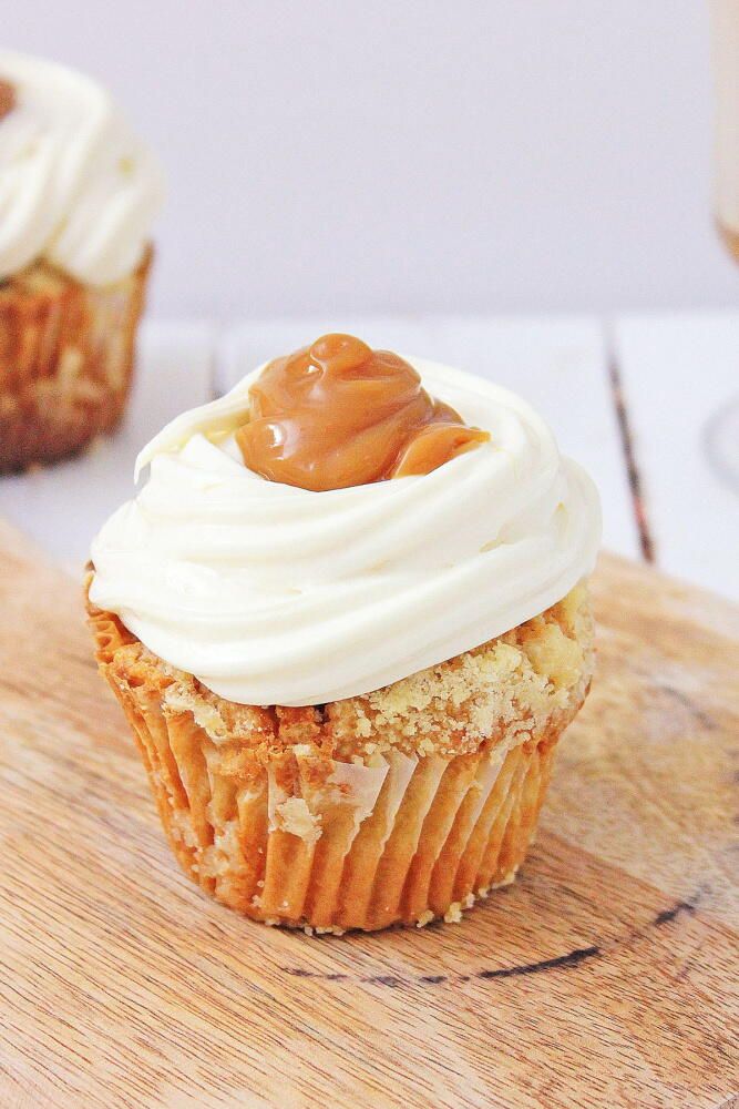 two cupcakes with frosting and caramel on top sitting on a cutting board