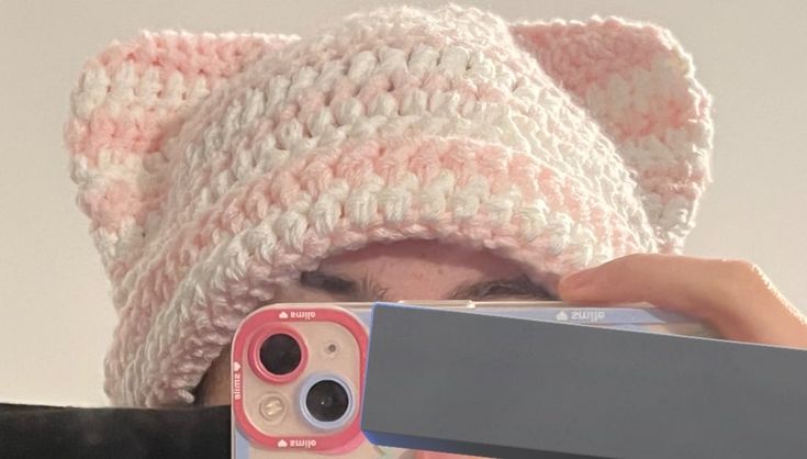 a woman taking a photo with her cell phone while wearing a knitted cat hat