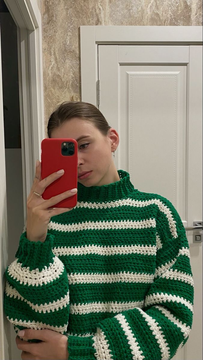 a woman taking a selfie with her cell phone in front of the door while wearing a green and white striped sweater