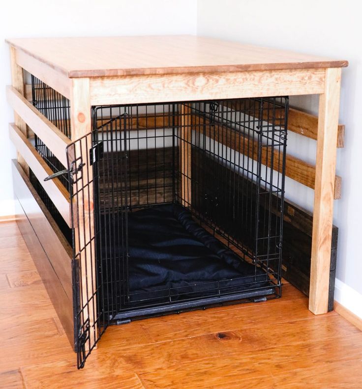 a dog crate with its door open on the floor next to a wooden table and stairs