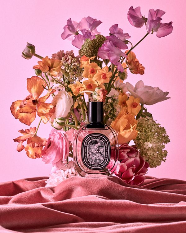 a bouquet of flowers sitting on top of a pink blanket next to a bottle of perfume