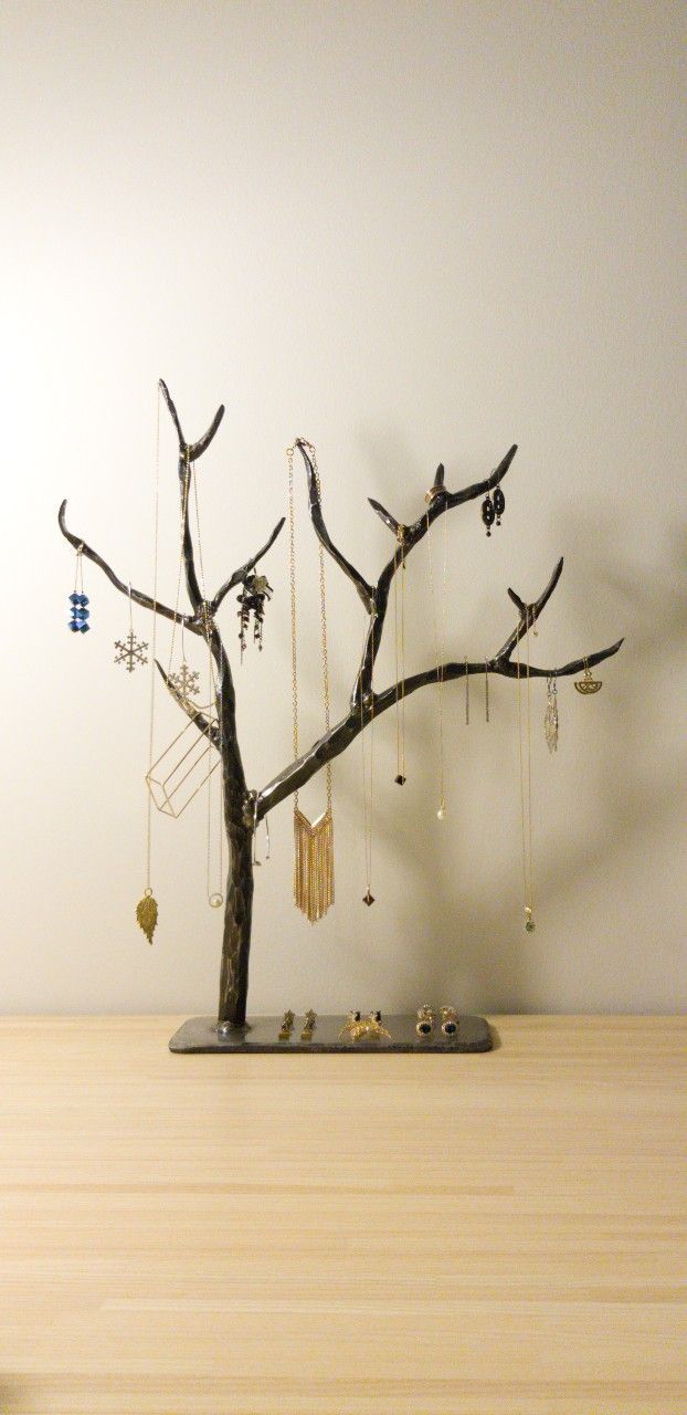 a small tree with jewelry hanging from it's branches in front of a white wall