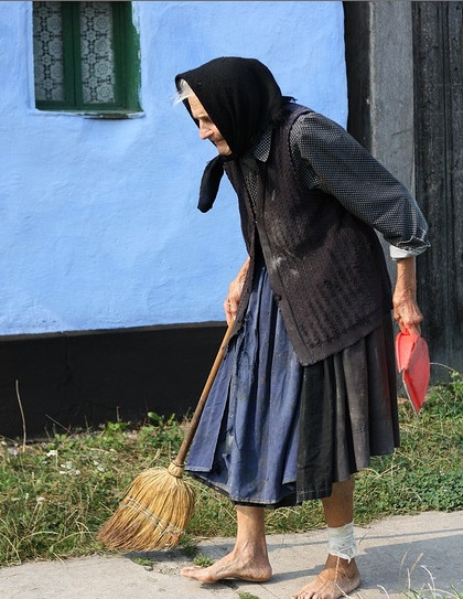 a woman with a broom is walking on the sidewalk in front of a blue building