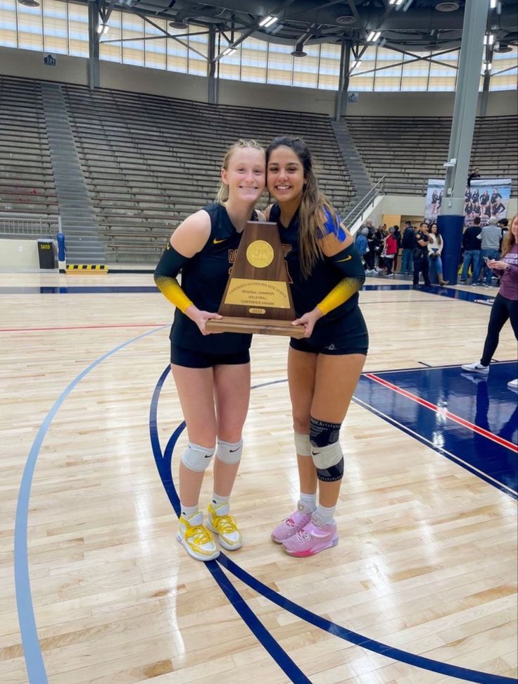 two female volleyball players posing with their trophy