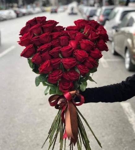 a bouquet of red roses held by someone on the side of the road with cars in the background