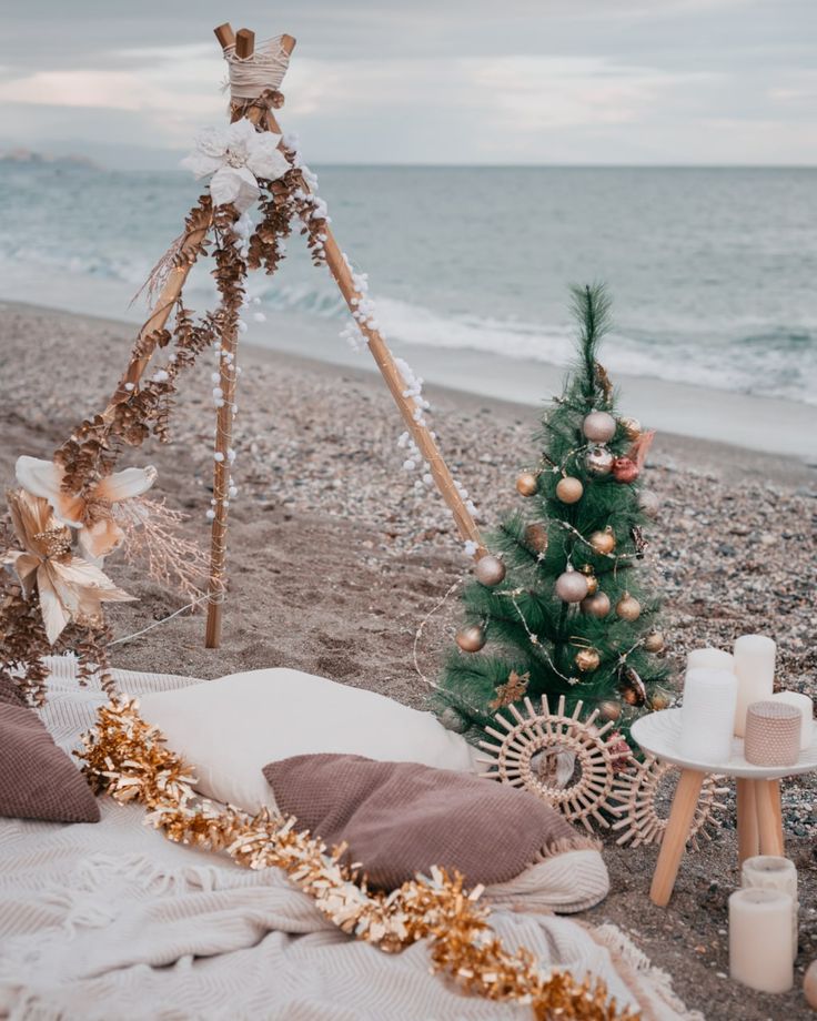 a christmas tree on the beach next to a teepeet with decorations and candles