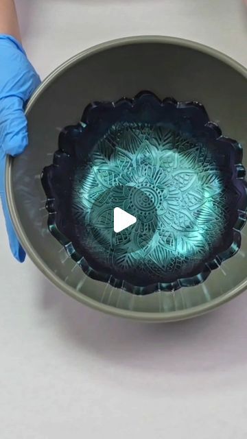 a person in blue gloves is holding a bowl with an intricate design on the inside