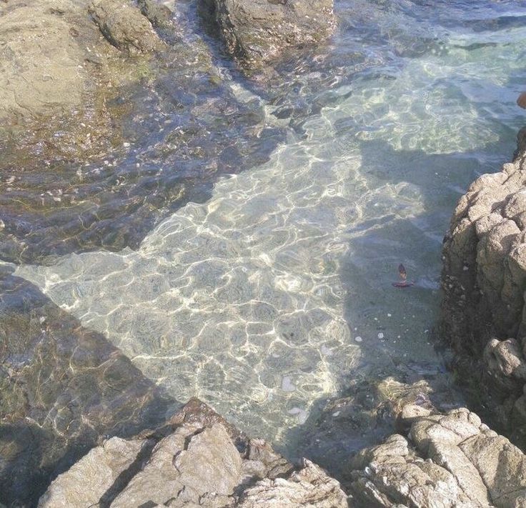 the water is crystal clear and there are rocks in the foreground with an orange object on it