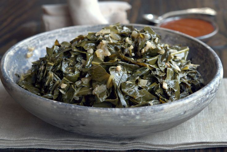 a white bowl filled with greens on top of a table next to some dipping sauce