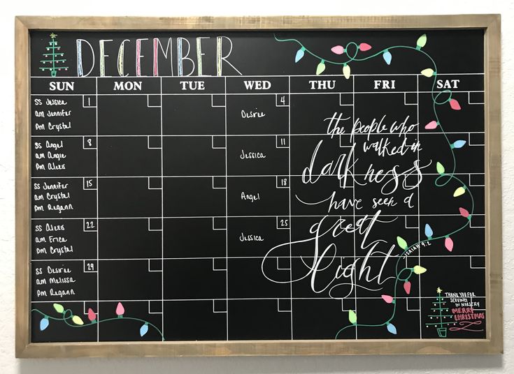 a chalkboard calendar hanging on the wall in front of a white wall with writing