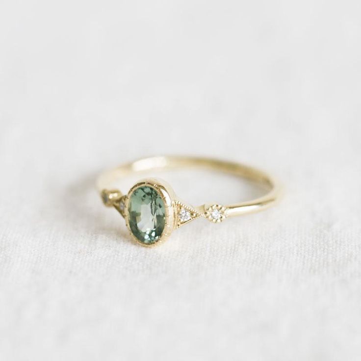 a gold ring with an oval green stone and two small diamonds on the side, sitting on a white surface