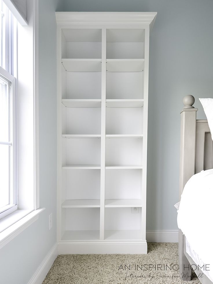 a white bookcase sitting next to a bed in a room with carpeted floors