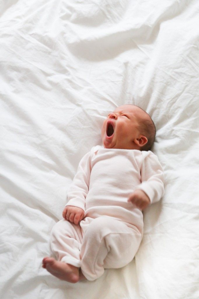 a baby yawns while laying on a bed