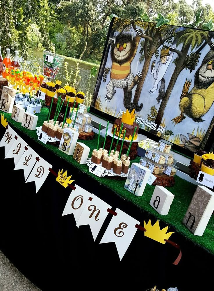 a table topped with lots of cupcakes and cakes next to a forest scene