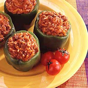 four stuffed peppers on a yellow plate with tomatoes