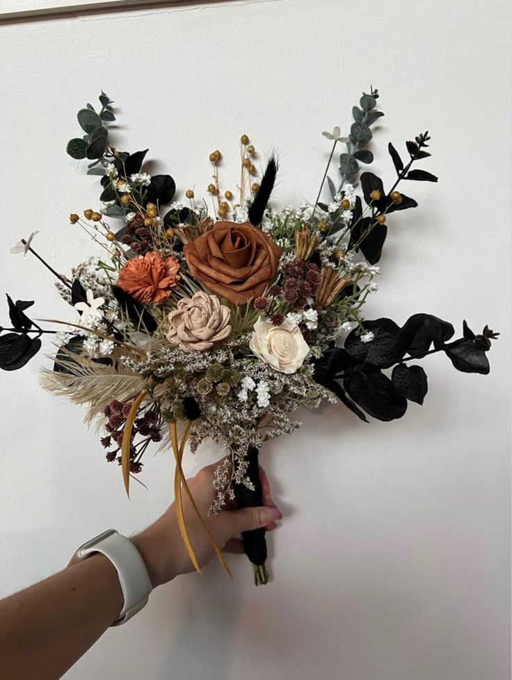 a person holding a bouquet of flowers in their left hand, against a white wall