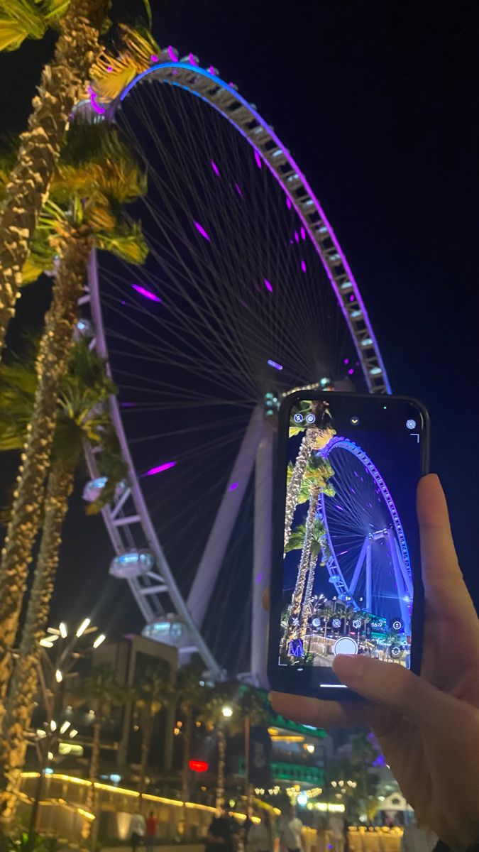 someone taking a photo of the ferris wheel at night with their cell phone in hand