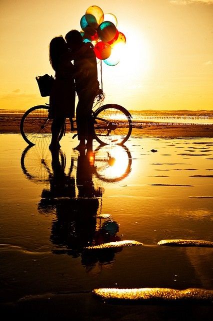 two people standing next to each other on the beach with balloons in front of them