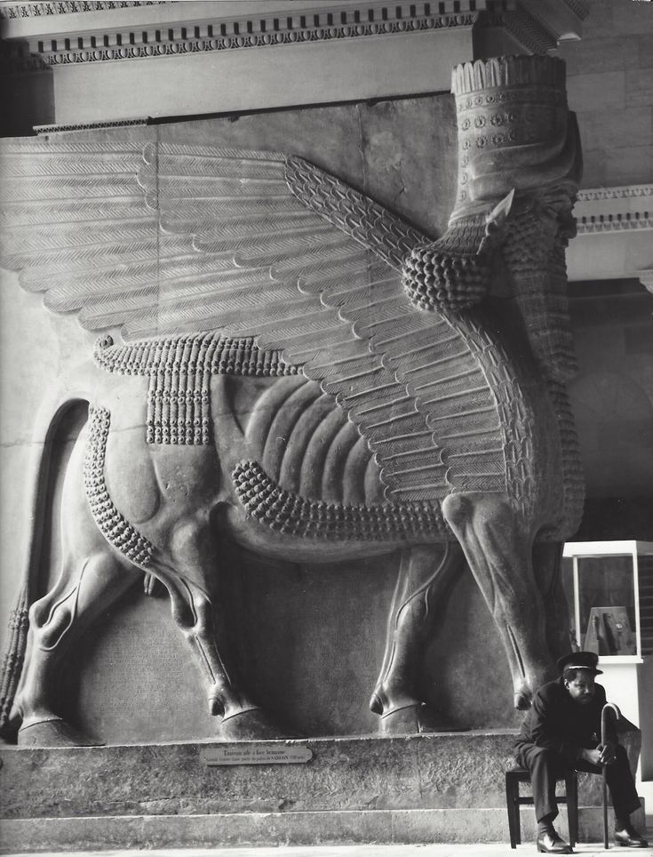 a man sitting in front of a statue of a bull with wings on it's back